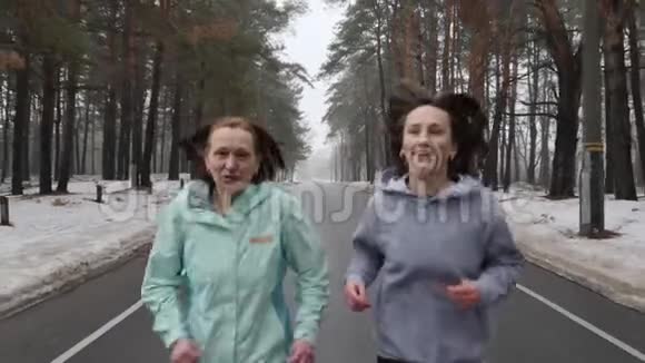 快乐的年长和年轻的高加索女人在冬天的雪地公园里奔跑交谈和微笑关闭前方跟随射击慢速视频的预览图