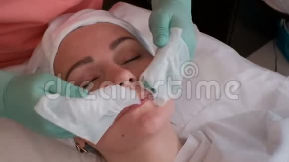 特写镜头美容师用湿巾擦着漂亮女孩的脸女人戴绿色手套振兴治疗视频的预览图