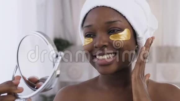 头上戴着白毛巾的漂亮非裔美国女人眼睛下面贴着金色的补丁看着视频的预览图