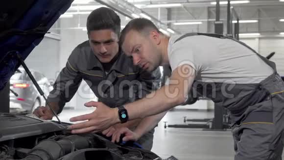 汽车机械师在他们的车库里讨论破车的问题视频的预览图