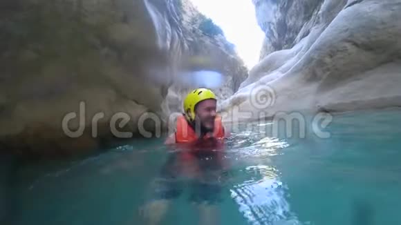 积极休息年轻快乐的男游客穿着防护服漂浮在水中的石头背景下抱着视频的预览图