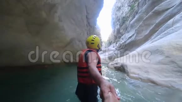 极限蜜月年轻快乐的男游客穿着防护服牵着手领着妻子在山洞里的水里漫步视频的预览图