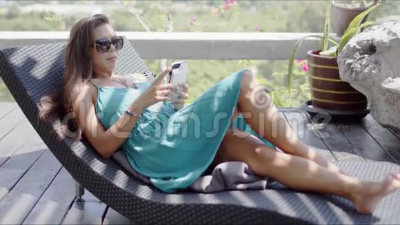 有魅力的女士带着智能手机在躺椅上休息视频的预览图