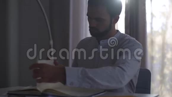 英俊的白种人在傍晚的阳光下坐在室内在笔记本上做笔记男性专业建筑师视频的预览图