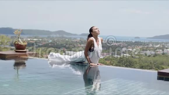 放松的女人在游泳池附近的美丽风景下做眼镜蛇宝宝运动视频的预览图