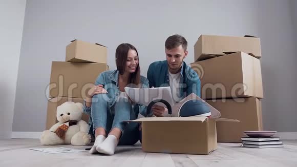 一对漂亮快乐微笑的夫妇坐在地板上为他们的新公寓规划更多的乐趣视频的预览图