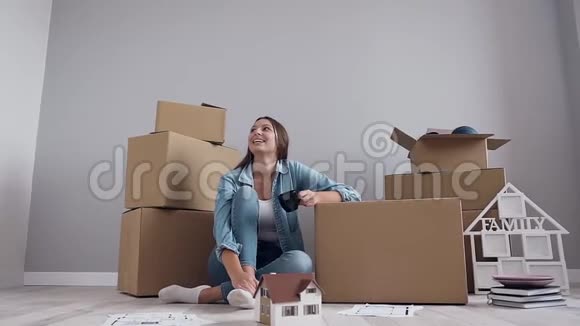 幸福微笑的漂亮女人坐在地板上喝着咖啡在新的当代公寓享受她的新生活视频的预览图
