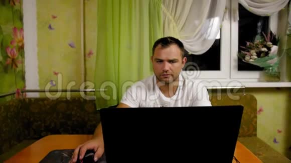 坐在家里的餐桌上坐在家里的男人用电脑看着显示器屏幕中弹视频的预览图
