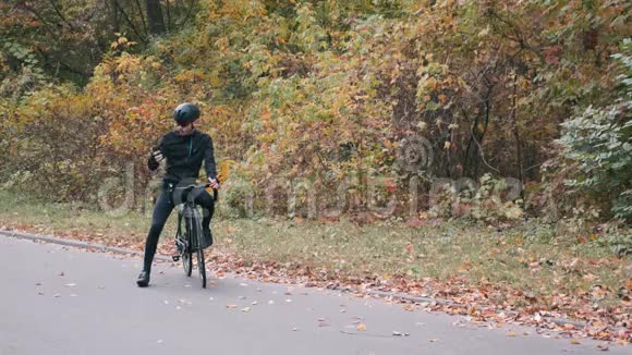 年轻英俊的职业三项运动员穿着黑色自行车服戴着黑色头盔戴着眼镜在秋林骑自行车视频的预览图