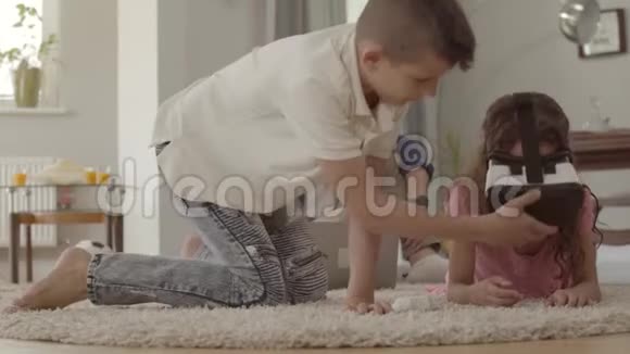 可爱的男孩和女孩躺在毛茸茸的地毯上用虚拟现实眼镜父亲坐在背景上视频的预览图