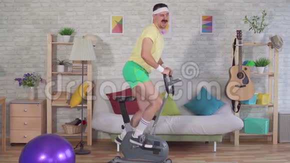 活泼开朗的男子运动员80留着胡子在家里骑着运动自行车慢悠悠视频的预览图