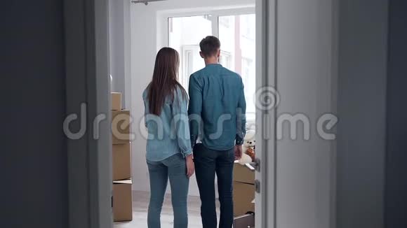 这对可爱的幸福夫妇站在窗前空荡荡的新公寓的中央拥抱视频的预览图