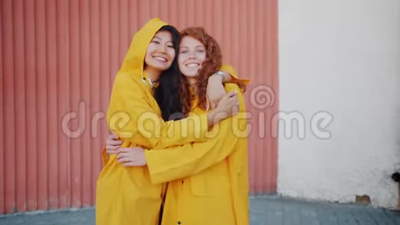 穿着雨衣拥抱和微笑看着户外摄像机的快乐年轻女性视频的预览图