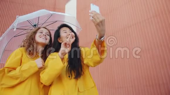 女孩在户外自拍智能手机拿着雨伞穿着雨衣视频的预览图