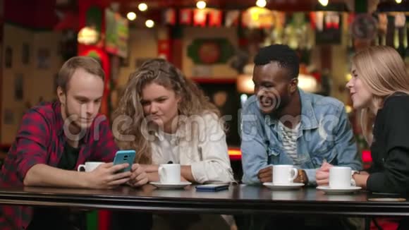 在酒吧里一群快乐的朋友一边喝着咖啡一边笑着讨论着看着智能手机屏幕视频的预览图