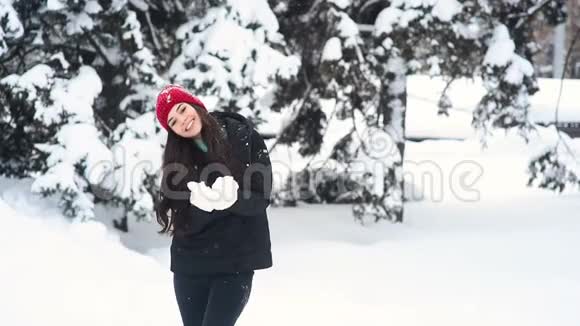 年轻可爱的女孩微笑着玩得开心在冬天的森林和白雪覆盖的树木的背景上扔雪视频的预览图