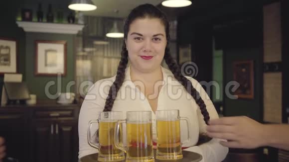 一个梳着辫子的女人穿着白色衬衫拿着托盘带着三个啤酒杯对着镜头微笑男人握手视频的预览图