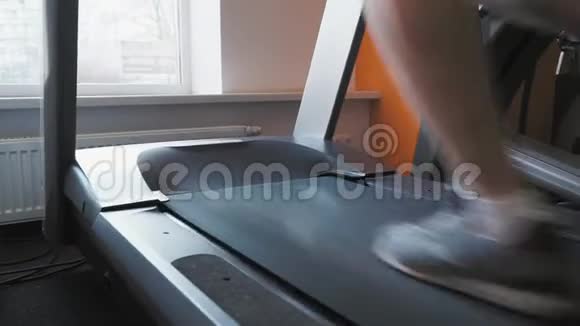 在健身室的跑步机上奔跑的无法辨认的男人的腿关闭背部低角度拍摄视频的预览图