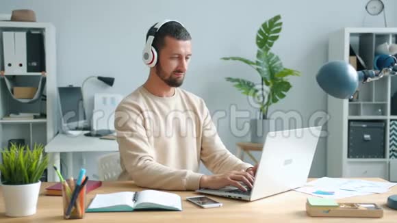 戴耳机的快乐青年用电脑办公用笔记本电脑视频的预览图