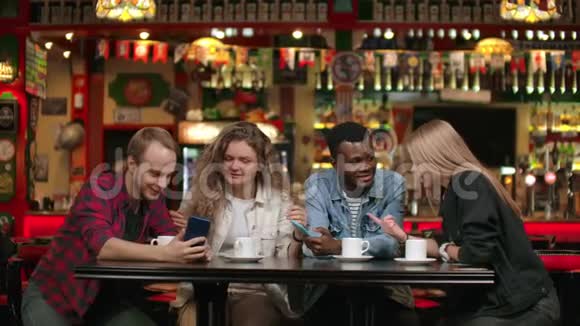 一群多民族的学生三个欧洲人和一个非裔美国人看着手机屏幕笑着讨论视频的预览图