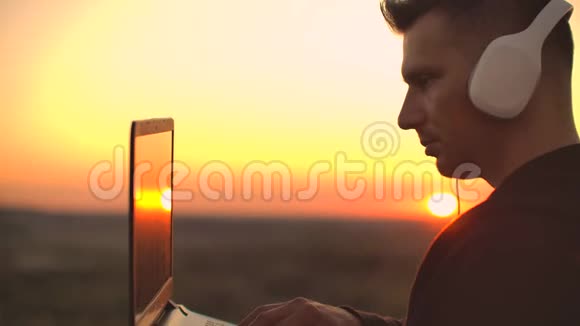 在日落时分站在屋顶上带着笔记本电脑和耳机里的啤酒可以远程工作欣赏美景处于视频的预览图