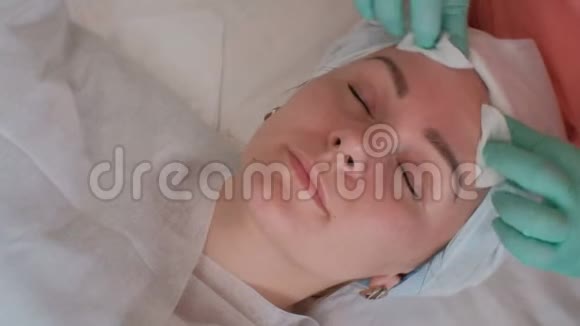 美容师用棉垫擦拭漂亮女孩的脸皮肤护理及皱纹处理一位欧洲美女视频的预览图