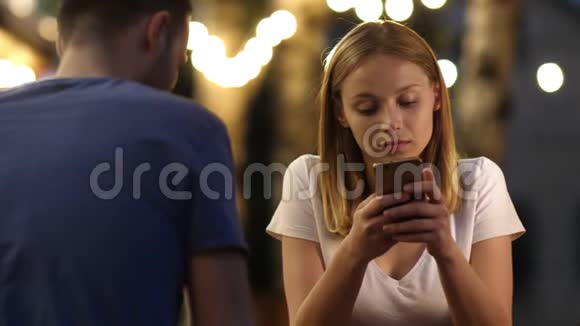 糟糕的约会中无聊的漂亮年轻女人用她的手机视频的预览图