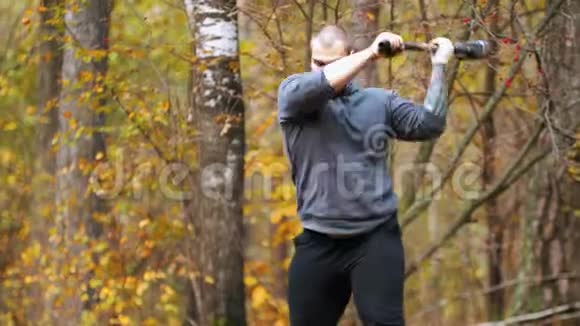 一个大个子健美运动员用金属锤击卡车轮胎秋天的森林视频的预览图