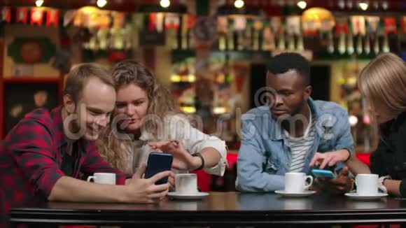 多民族夫妇坐在咖啡馆里通过电话看屏幕并在电话磁带中翻阅照片视频的预览图