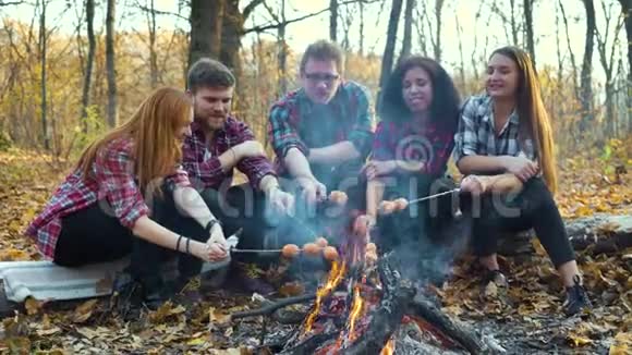快乐的游客在秋天的森林里烤香肠篝火过火视频的预览图