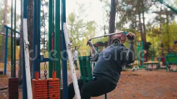 一名男子健美运动员在户外运动场上训练拉与重量相连的酒吧秋天的森林视频的预览图