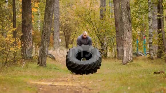 一个大个子健美运动员在地上翻过轮胎并向前移动在秋林户外训练视频的预览图