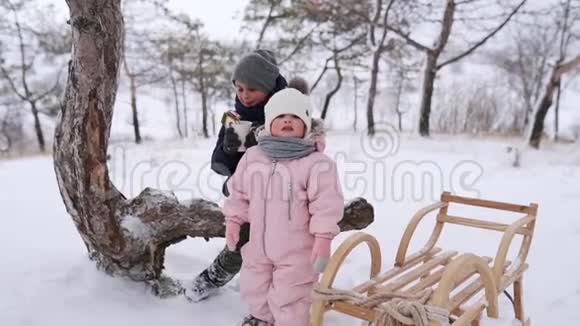 穿着粉红色连衣裙的男孩和小女孩在雪天滑雪后玩得很开心兄弟姐妹过冬视频的预览图