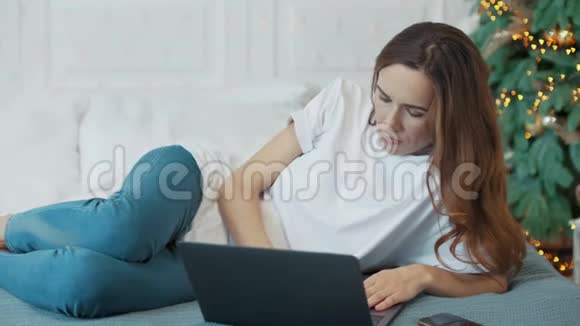 集中休闲的女人在卧室里躺着笔记本电脑视频的预览图