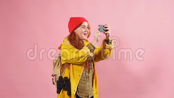 一个戴着黄色雨衣的红头发快乐女孩用智能手机拍摄的工作室画像视频的预览图