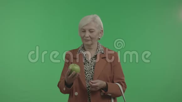 老年女性在绿色背景下审视手中的苹果视频的预览图