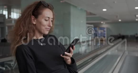坐自动扶梯的女人在国际机场拿着行李用手机视频的预览图