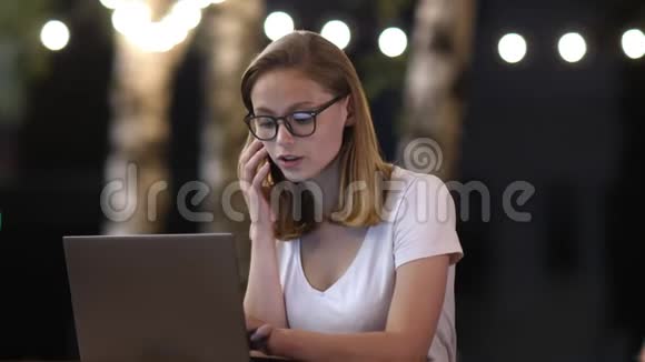 有魅力的年轻女性在笔记本电脑上工作时会有智能手机对话视频的预览图