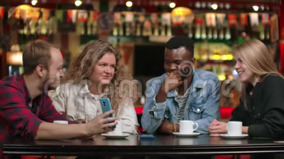 一个非洲裔美国男人一个女孩看着智能手机一边坐在咖啡里一边喝咖啡一边说话视频的预览图