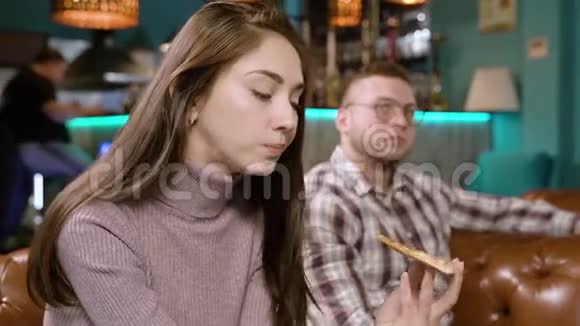 年轻迷人的女人在咖啡馆里吃比萨饼和和朋友聊天视频的预览图