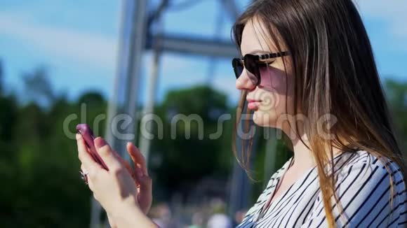 戴墨镜的美丽女游客的肖像在桥上使用智能手机视频的预览图