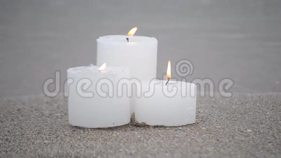 三支白色小蜡烛在沙滩岸边燃烧视频的预览图