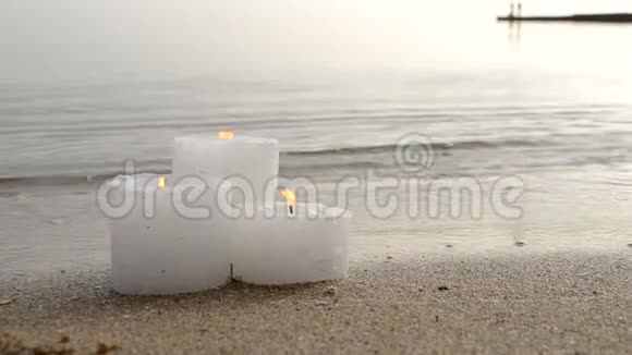 三支白色小蜡烛在沙滩岸边燃烧视频的预览图