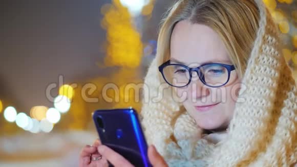 一位年轻女子晚上在雪地街道上使用智能手机的肖像视频的预览图