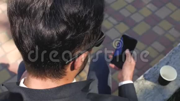 时髦的男人穿着经典的西装和太阳镜坐着看手机从上面看有电话的商人4k4k视频的预览图
