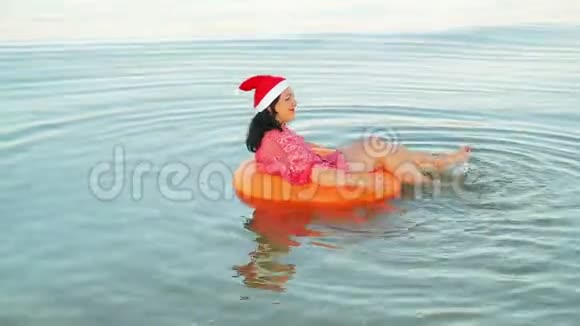 游泳圈里的一个黑发女人和一顶圣诞老人的帽子在海上度过圣诞节和新年视频的预览图