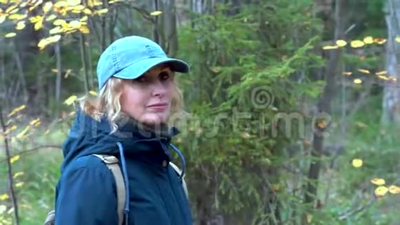 一个身材苗条的漂亮女人背着一个背包戴着一顶帽子走在秋天的森林里在桦树和枞树之间视频的预览图