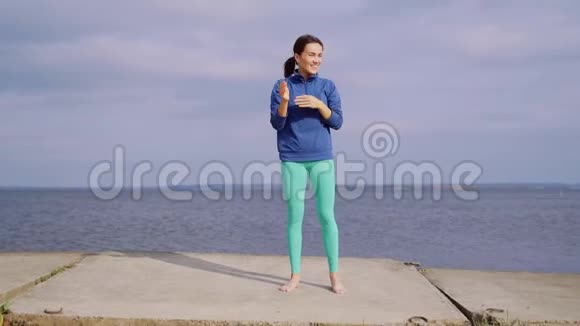 女孩站在河边的水泥板上做伸展运动户外运动视频的预览图