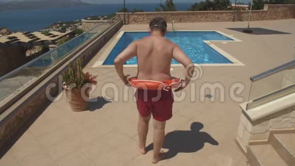 穿着橙色救生圈和红色游泳短裤的男人跳到游泳池视频的预览图