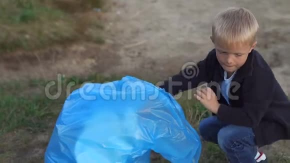一个小男孩在公园里的河边或湖边的海滩上收集垃圾视频的预览图